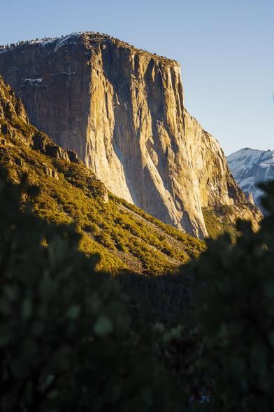 A close-up of a large granite cliff illuminated by sunlight, showcasing its rugged texture and steepness.