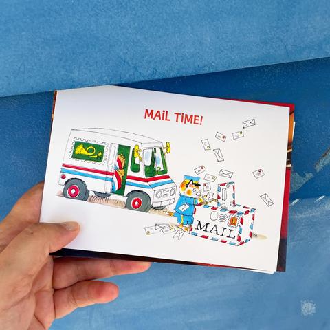 Hand holding a postcard in front of a blue mailbox. The postcard illustration shows a mail truck and a cartoon animal postal worker surrounded by flying envelopes, with the words “MAIL TIME!” at the top.