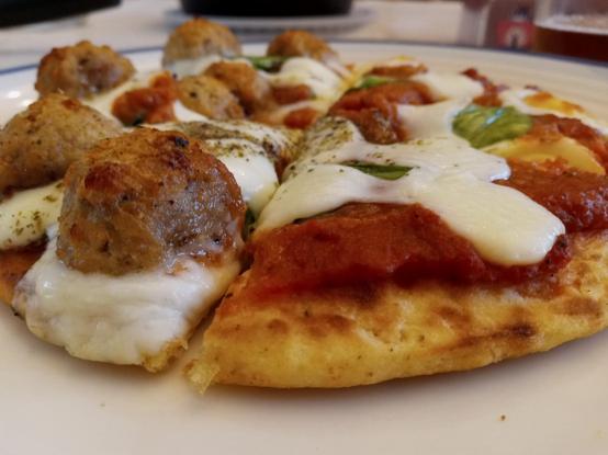 Photo, from a low angle, of the above-described pizza, rich with sauce, melted mozzarella, and toasted meatballs on the left half, with a cheeky bit of spinach peeking through.