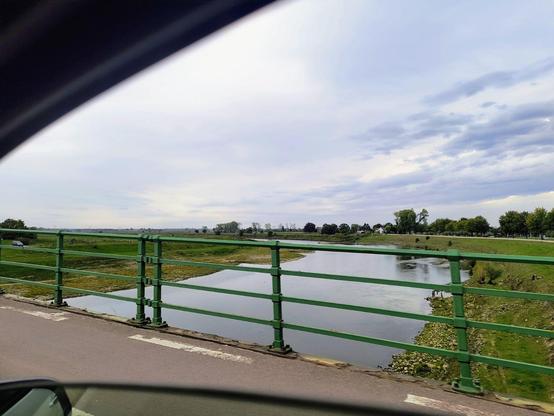 Auf dem Bild ist der Blick aus dem #Aixam zu sehen, wie ein Kanal auf einer Brücke mit grünem Geländer überquert wird.