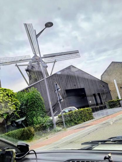 Auf dem Bild ist der Blick links aus dem Aixam festgehalten, zu sehen ist eine schwarze Scheune, hinter der eine Windmühle zu sehen ist