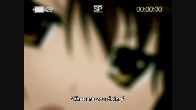 A blurry image of a girl (Haruhi) seen through the viewfinder of a 4:3 camcorder saying, "What are you doing?"