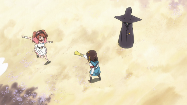 A girl (Mikuru) is striking a pose that another girl (Haruhi) is telling her to do while another girl (Yuki) stands in the background in a witch costume.