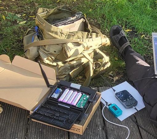 Rucksack, Wiese, mehrere Geräte mit Antennen. Ein Fuß ragt ins Bild.