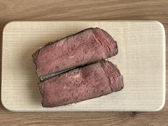 Zwei dünne Scheiben rosa gegrilltes Rindfleisch als Aufschnitt auf einer Scheibe Brot, bestreut mit etwas Salz und Pfeffer 