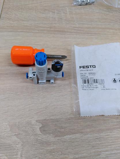 Cute little pressure regulator with a grey plastic body and blue adjuster knob. Behind it, to show its size, a small screwdriver with an orange handle.