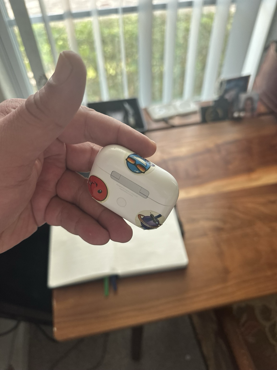 My hand holding AirPods case with three smiley face stickers