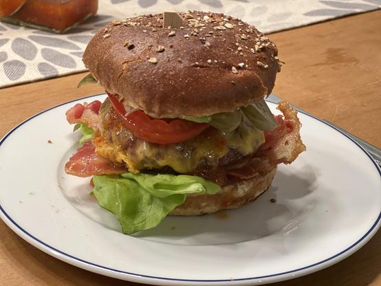 Ein Burger, fertig zum rein beißen:

Belegt mit Salat, Bacon, Käse, Tomaten, sauren Gurken und Oma-Dadmins hausgemachter Chilisauce. 

Alles wird von einem Holzspieß in der Mitte zusammen gehalten, der jedoch für diesen schiefen Turm von Weber etwas kurz geraten ist. Er ragt kaum aus der oberen Brötchenhälfte heraus 