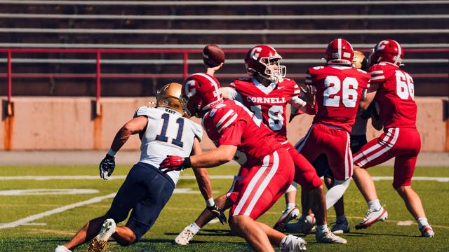 Number 11 in white, blue and gold sneakers behind the line defending quarterback Number 18 who's in the process of making a pass