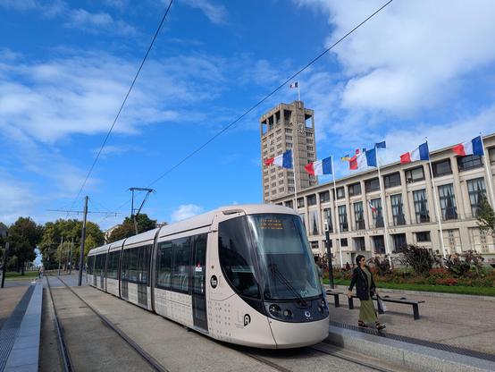 Tramway direction "La Plage" devant l'hôtel de ville du Havre, drapeaux français flottent sur la place et la tour de l'hôtel de ville