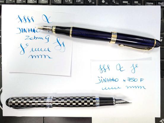 Dwa pióra i dwie małe karteczki z maziajami i napisami wykonanymi tymi piórami. Jedno u góry to Jinhao 450 ze stalówką Zebra G, elastyczną pozwalającą nacismiem zmieniać szerokość linii. Jest granatowe ze złotymi akcentami.

Na dole Jinhao x750 w czarno-srebrną szachownicę ze stalówką F