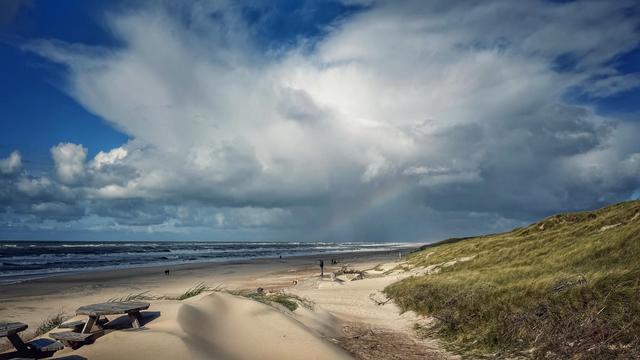 Strandansicht mit einer großen Wolkenformation samt Teil eines Regenbogens. 
