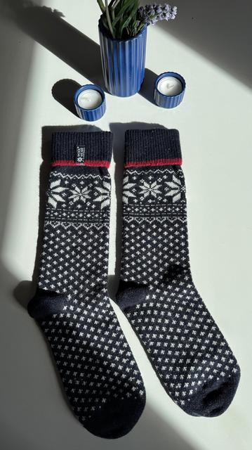 Dunkelblaues Paar norwegische Wollsocken mit typischem Muster liegen auf einem weißen Tisch und werden seitlich von der Sonne angestrahlt. 