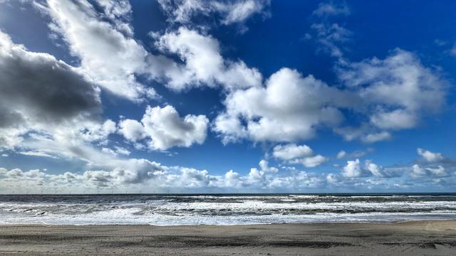 Strandansicht mit rauschender Brandung, blauem Himmel und ein paar weißen Schäfchenwolken. 
