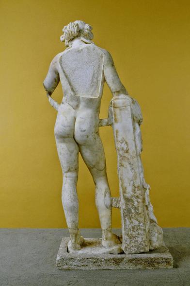 A marble sculpture of Dionysos seen from the reverse side. A part of his back has broken off.