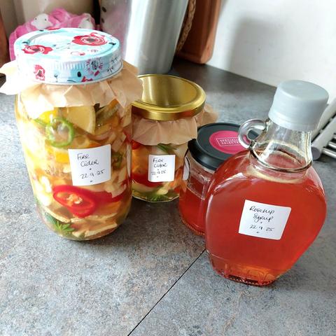 A grey counter top with two jars of fire cider, a half full jar and a full small bottle of rosehip syrup.