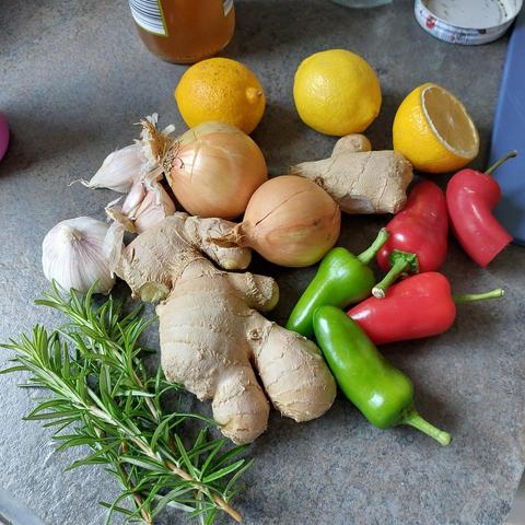 Lemons, chillies, onions, ginger, garlic, and sprigs of rosemary on a grey counter top.