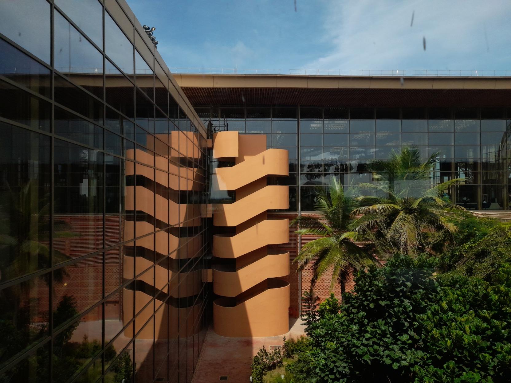 A view of part of an outdoor garden as seen from the upper level of Terminal 2 of Bangalore's Kempegowda International Airport. Behind the garden lies a flight of stairs with tall beige walls, all the way from the ground to the top level of the terminal building.