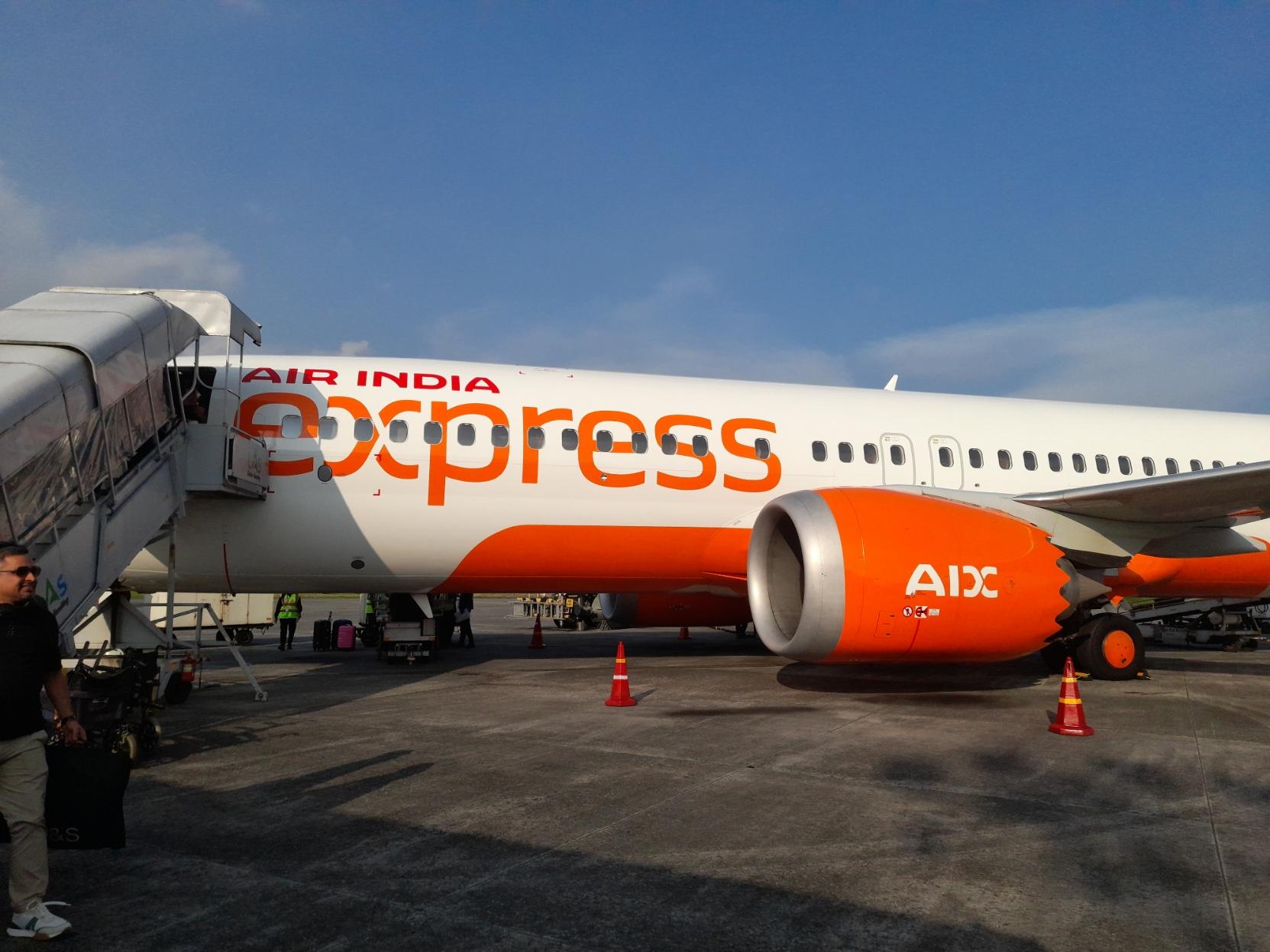 A Boeing 737-800 in the new Air India Express livery, parked on the apron with boarding stairs attached on its front left door on a late afternoon at Bagdogra Airport.