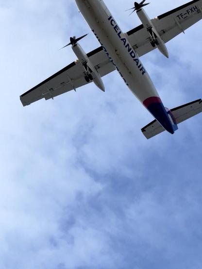 An Icelandair Dash-8 is seen up close from below. There are clouds above and the plane isn’t completely in frame. 