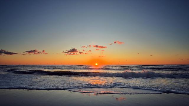 Sonnenuntergang an einem Strand. In den Wellen spiegelt sich das Sonnenlicht. 