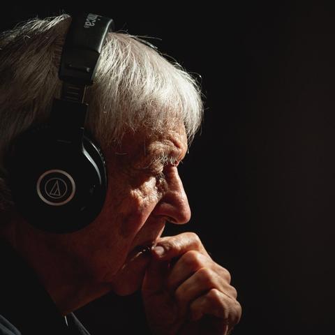 Le jazzman Michel Portal porte un casque audio noir, très concentré sur ce qu'il écoute.