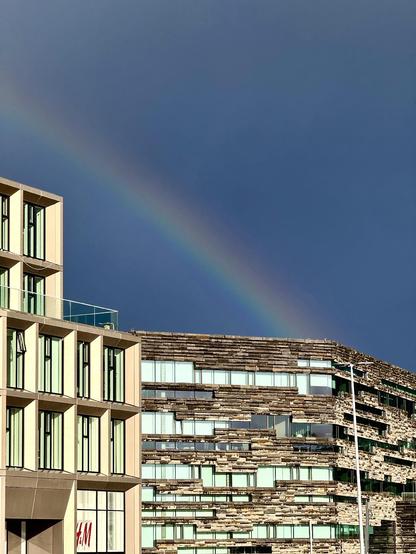 A rainbow can be seen behind the  Landsbankinn building in downtown Reykjavík. Very dark clouds behind it. 