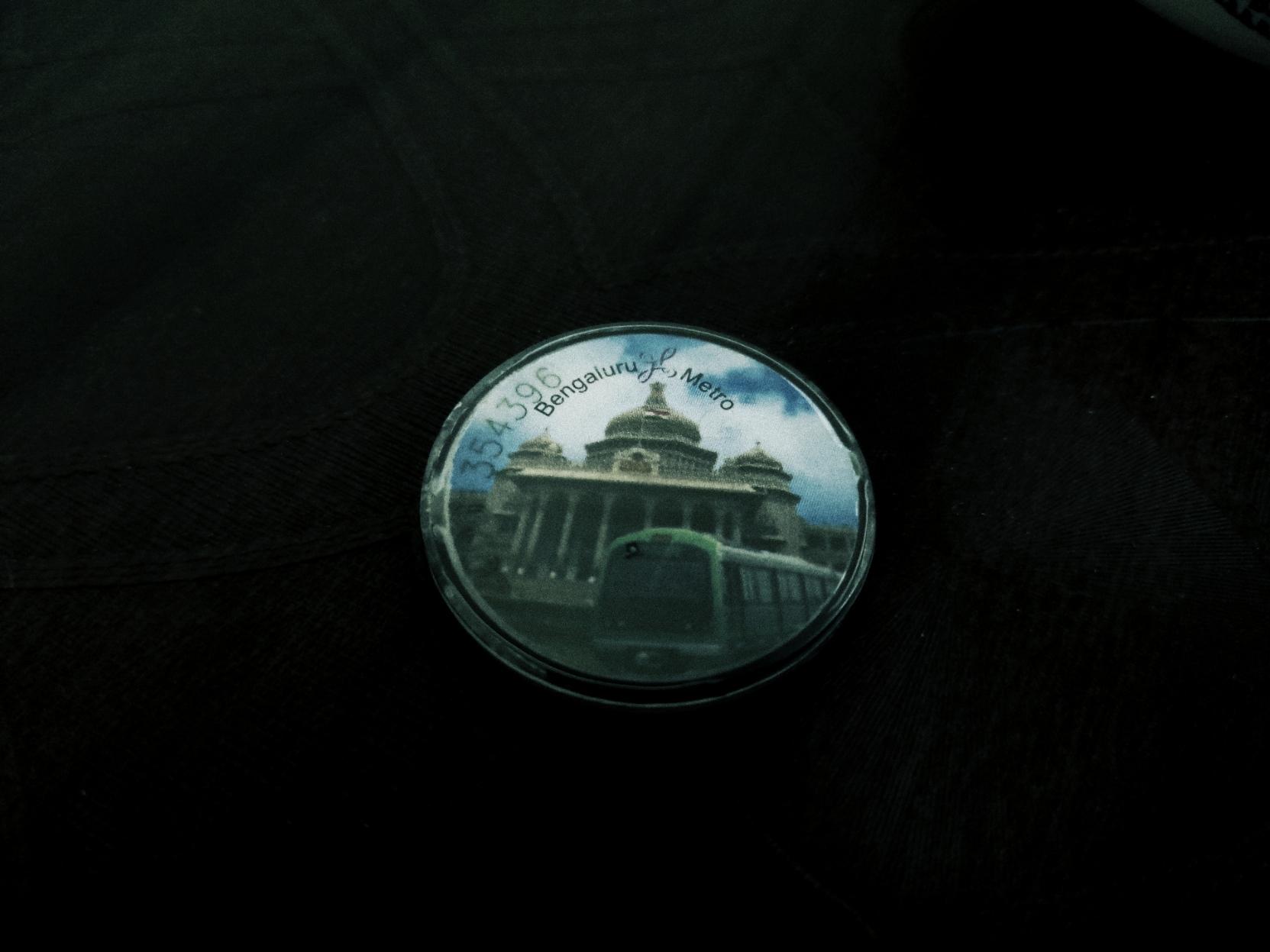 A token from Namma Metro's green line, featuring the logomark at the top of an image of the front of the Vidhana Soudha (Karnataka's Unicameral State Legislature), and a cutout of the green line's metro rake with a matching green accent. A token from Namma Metro's green line, featuring the logomark at the top of an image of the front of the Vidhana Soudha (Karnataka's Unicameral State Legislature), and a cutout of the green line's metro rake with a matching green accent.