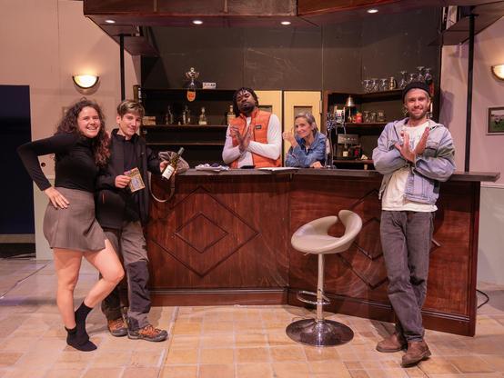 5 personnes posent dans un décors de théâtre ressemblant à un bistrot de campagne