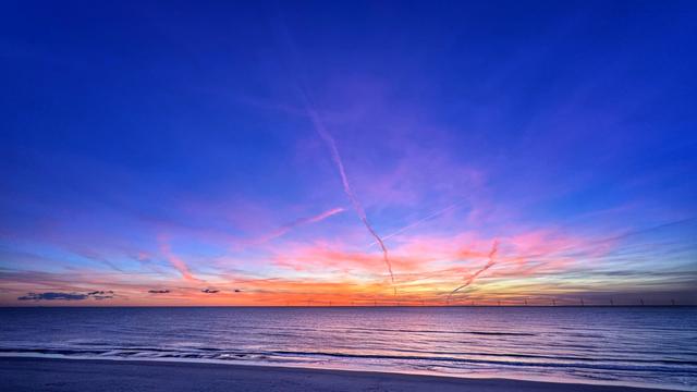 Buntes Farbenspiel am Himmel an einem Nordseestrand kurz nach Sonnenuntergang. Das Meer reflektiert die Farben, die aus Orange, Gelb und Rosa langsam in den dunkelblauen Himmel verschwinden. 