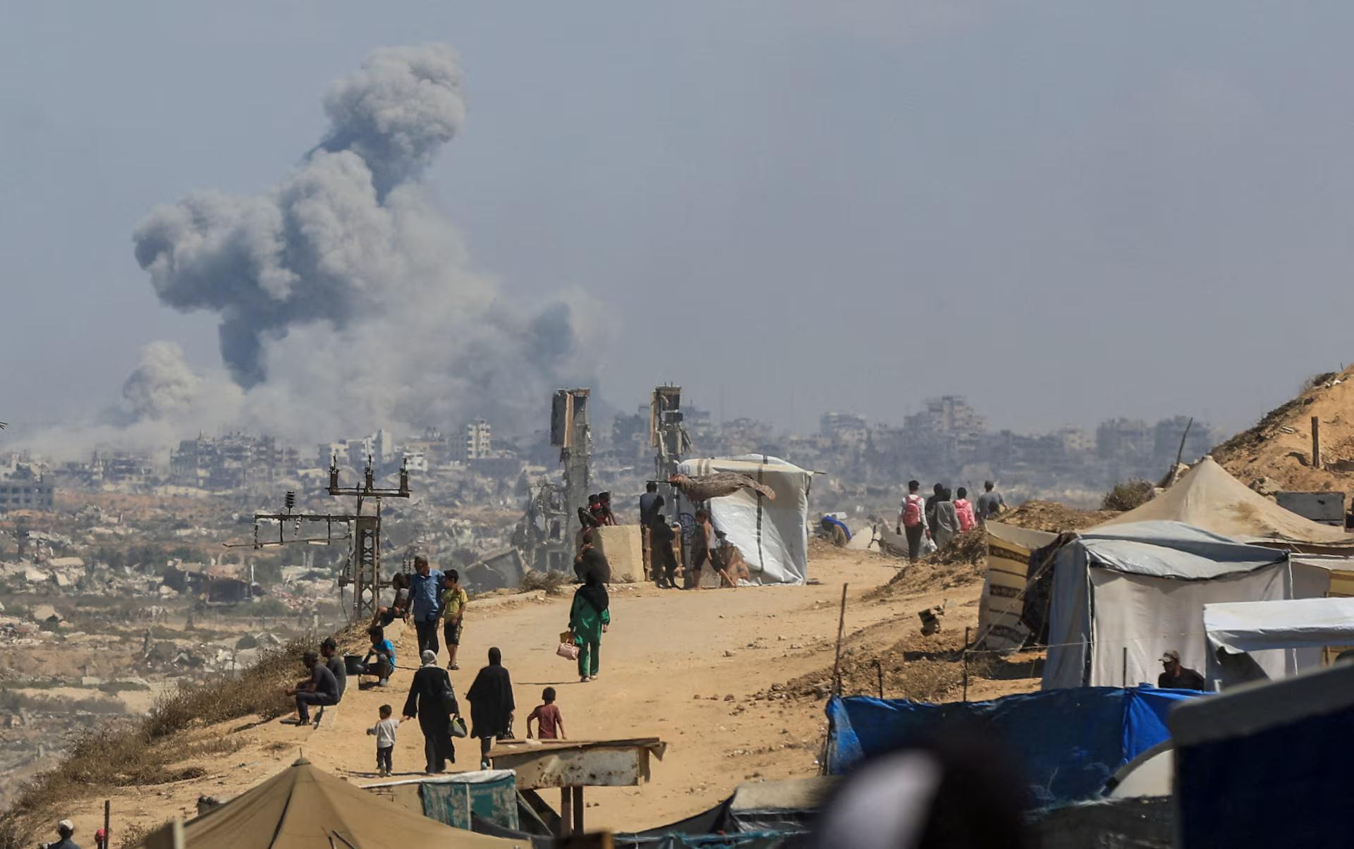Smoke rises from an Israeli strike, as displaced Palestinians, fleeing northern Gaza due to an Israeli military operation, move southward.