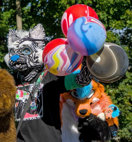 Ende der Fursuitparade, Katzenfursuiter hat Balloons und ein Fuchfursuiter mit einem Plüsh von sich selbst schaut unter die Balloons