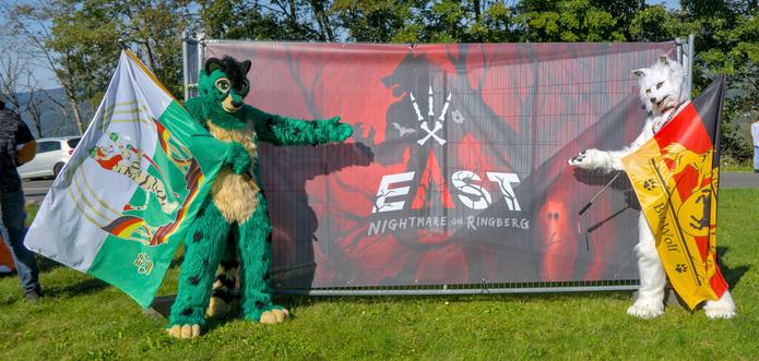 Grüner Katzenfursuiter mit Flagge und weißer Wolf Fursuiter mit Flagge zeigen das EAST 13 Logo