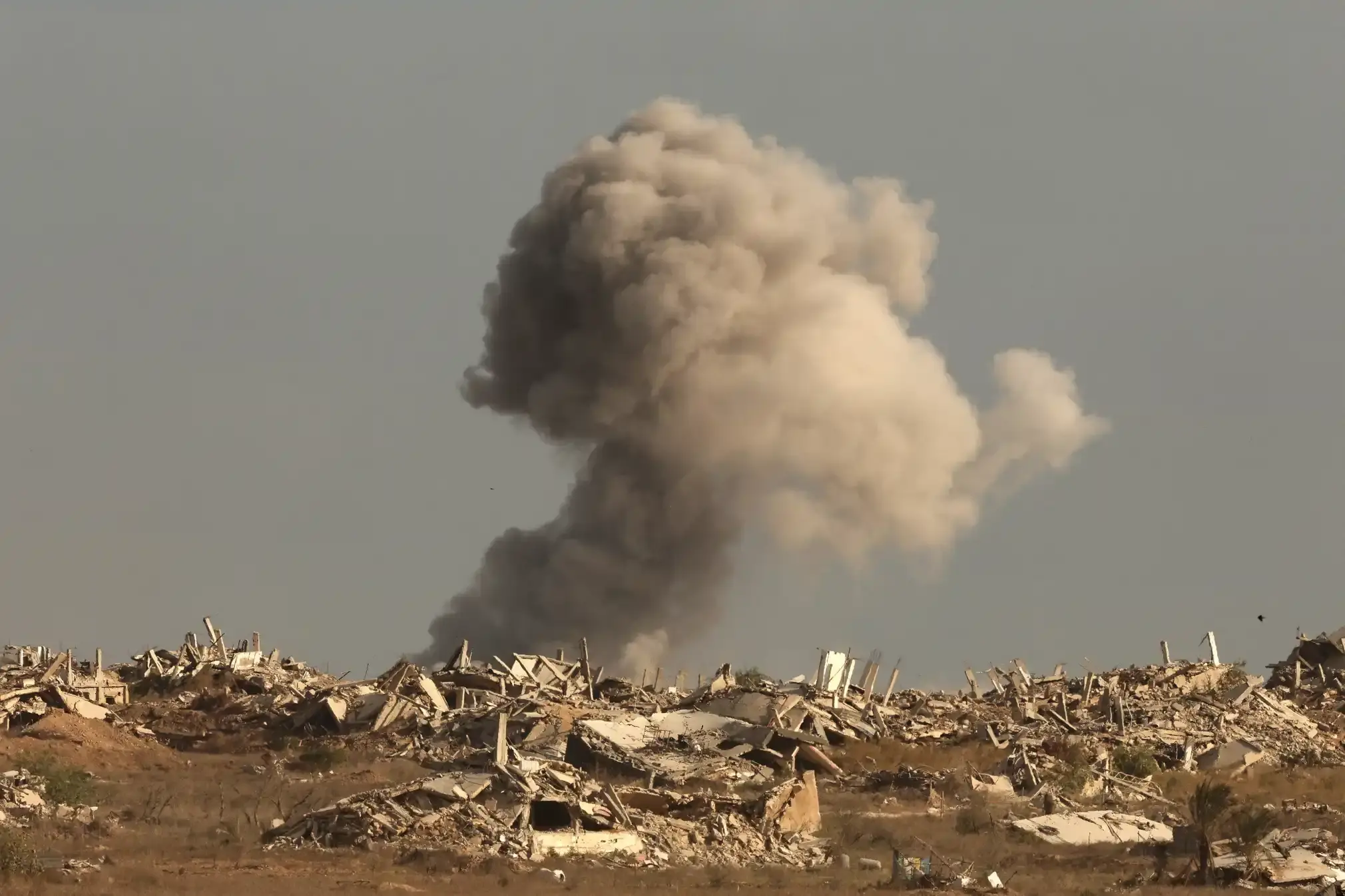 Smoke billowing after an Israeli attack in a lifeless environment with nothing but rubble & a buried car.
