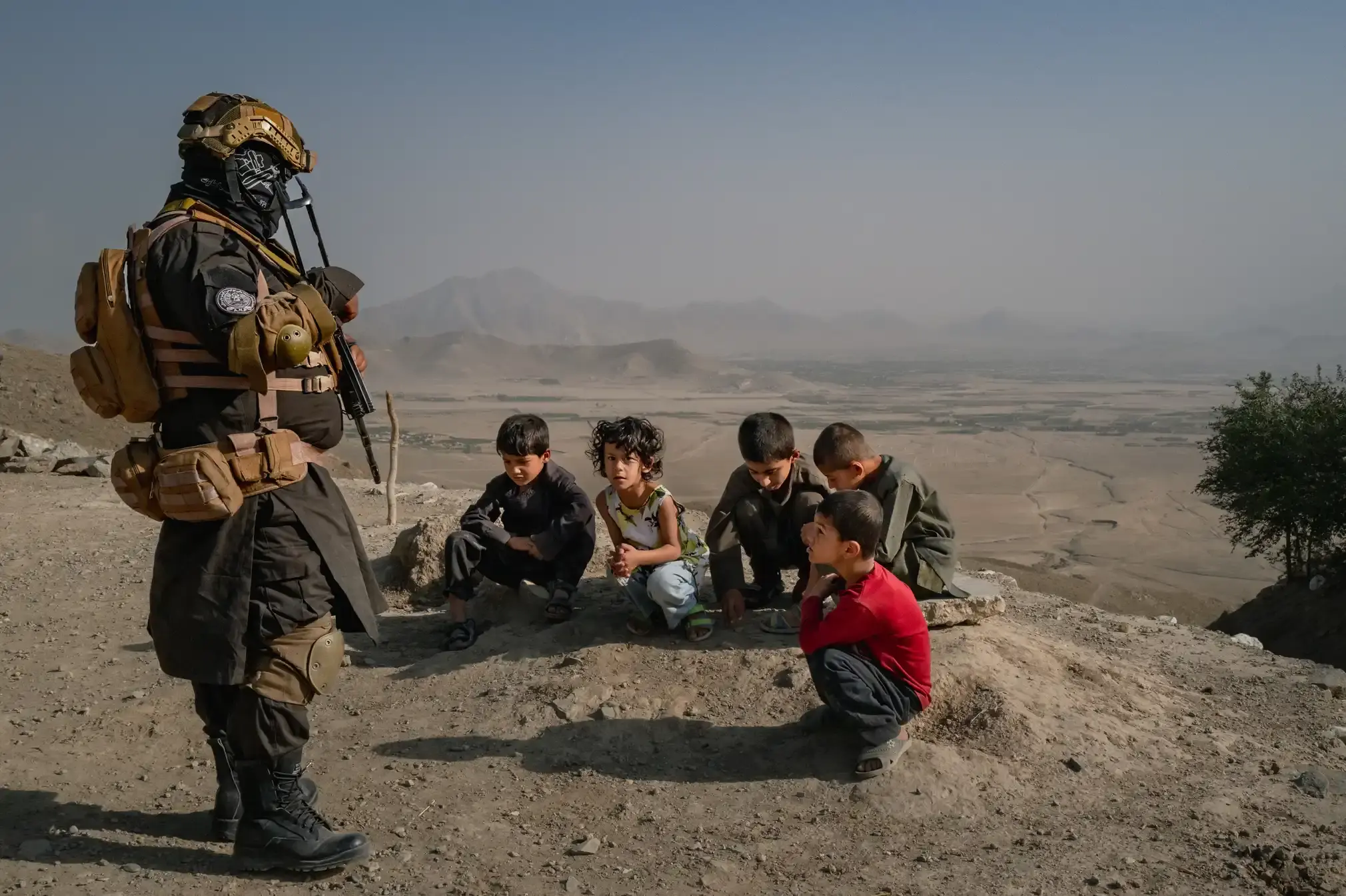 A police officer watches as children play in the dirt.