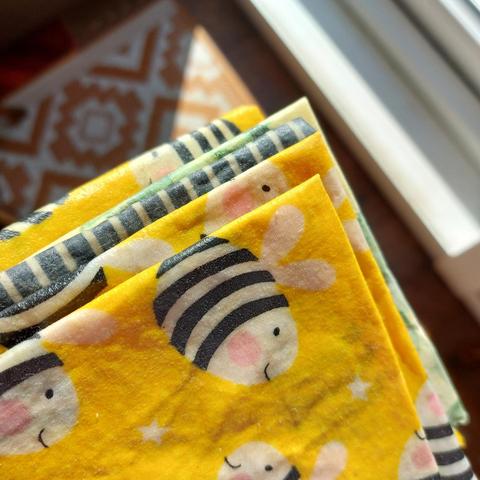 A little stack of waxed fabric squares, including the foremost one which is of large cartoon bees on yellow.