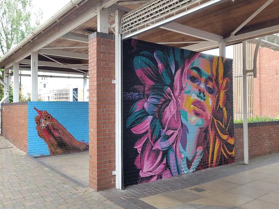 A mural of a Hen's face peeks out from behind a mural of a Woman's face surrounded by psychedelic flower petals