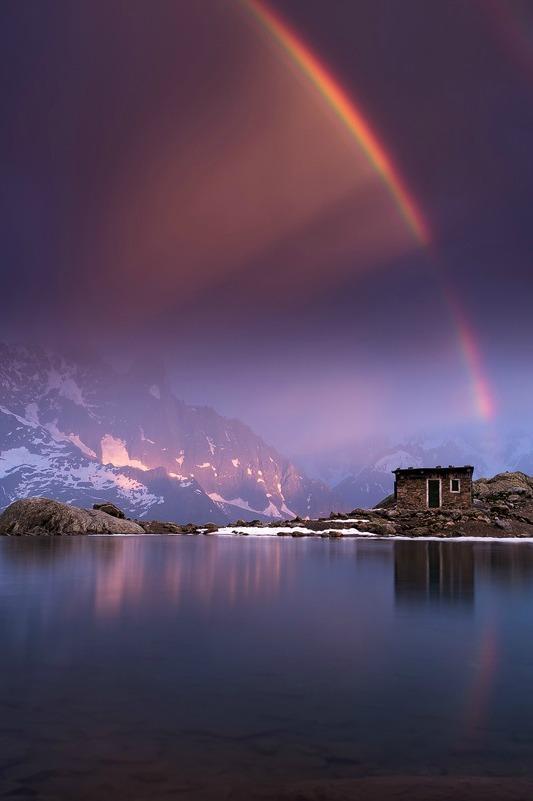 An intense rainbow over a snowy cliffside & water.