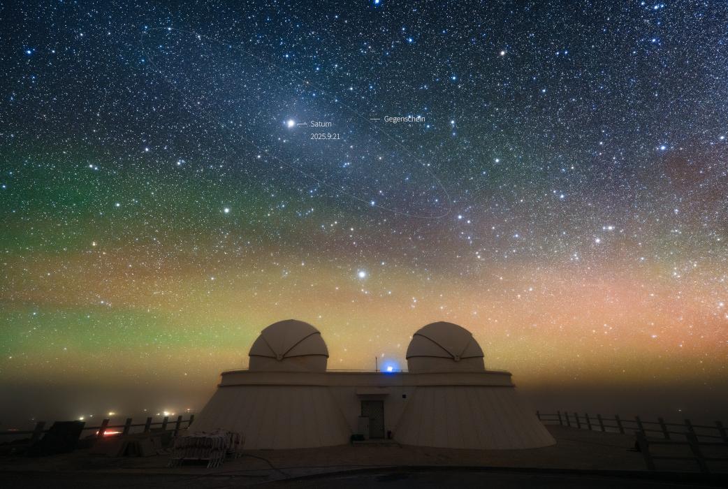 In this snapshot from the Qinghai Lenghu Observatory, Tibetan Plateau, southwestern China, the outer planet is immersed in a faint, diffuse oval of light known as the gegenschein or counter glow. The diffuse gegenschein is produced by sunlight backscattered by interplanetary dust along the Solar System's ecliptic plane, opposite the Sun in planet Earth's sky. Like a giant eye, on this dark night Saturn and gegenschein seem to stare down on the observatory's telescope domes from their antisolar perspective. Strong, atmospheric airglow forms a colorful background along the horizon.