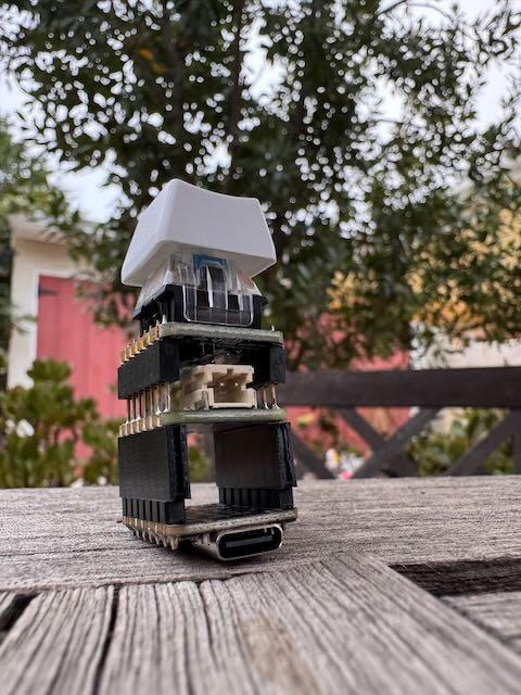 A small tower of three stories. The bottom level being the seeed Xiao, which one can tell from the USB-C port, the middle one the Adafruit battery BFF, and the top of the spire is a white key cap.