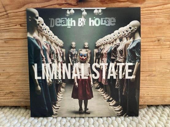 Ein Albumcover, das ein Kind mit clownsartigem Make-up zeigt, das zwischen Reihen von Schaufensterpuppen steht. Der Titel "LIMINAL STATE" prangt am unteren Rand, über dem Namen "Death By Horse". Der Hintergrund hat eine dunkle, unheimliche Ästhetik.