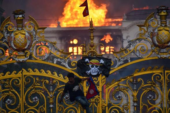 Hanging a One Piece game /pirate flag on the gates as smoke and flames rise after people set fire to the Singha Durbar, the seat of Nepal government's various ministers offices in Kathmandu, Nepal on September 9, 2025. 
Photo: Sunil Pradhan/Anadolu 