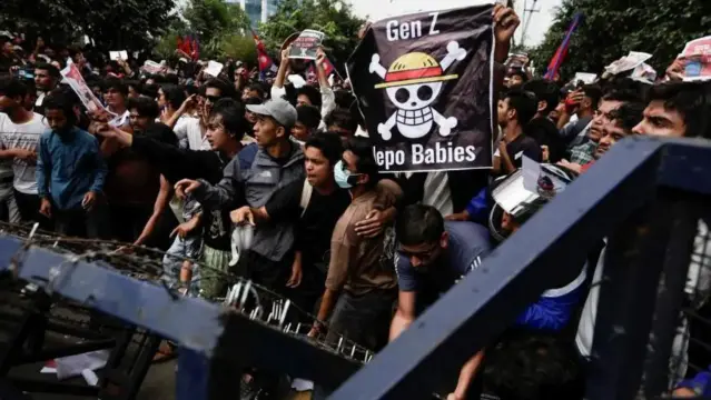 GEN Z 
NEPOT BABIES 
Banner with One Piece game / pirate flag on barricade with crowd outside 
the Singha Durbar, the seat of Nepal government's various ministers offices in Kathmandu, Nepal 
