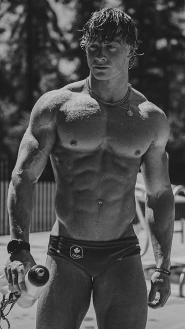 A black and white photo of muscular man wearing only a pair of briefs which bears the maple leaf logo of the Canadian flag and the Olympics logo