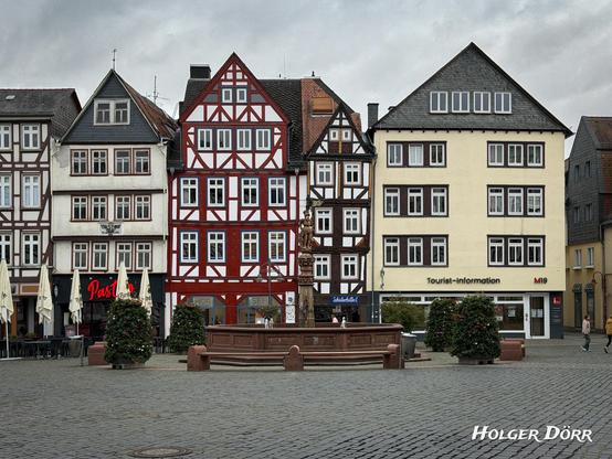 Weitwinkelaufnahme des Butzbacher Marktplatzes mit Brunnen in der Mitte, umgeben von Fachwerkhäusern.