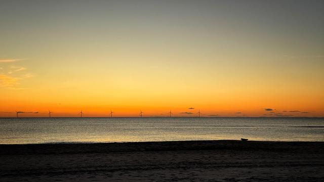Nach Sonnenuntergang an einem Nordseestrand: Der Himmel besteht aus einem orange-gelb-grauen Farbverlauf. Beim Übergang zum Wasser ist rechts eine dunkle Silhouette eines Seehunds am Strand zu sehen. 
