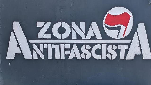 "Zona Antifascista" in white block capitals against a black background, with a logo of red and black flags