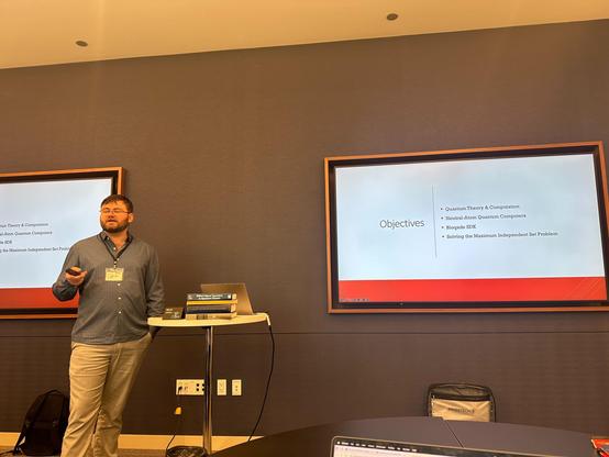 I stand lecturing over the objectives of the workshop. We start by learning quantum theory & computation, then dive into neutral-atom quantum computers followed up with an introduction to the Bloqade SDK, and finally solving the maximum independent set.