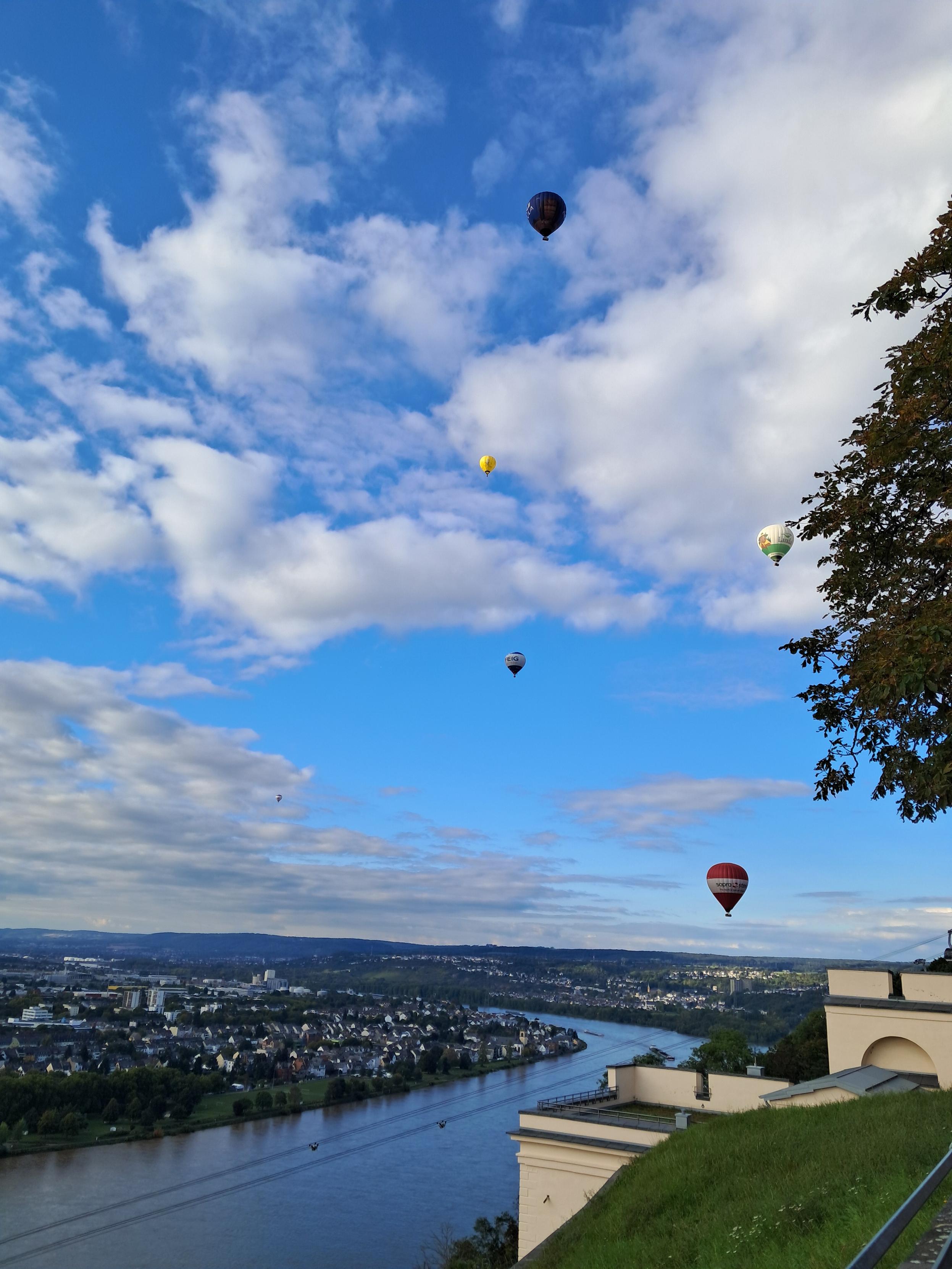 Blick auf Koblenz und auf den Rhein, darüber schweben fünf Heißluftballons