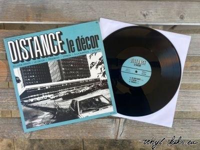 Ein Albumcover mit dem Titel "DISTANCE le décor" wird neben einer schwarzen Schallplatte gezeigt. Das Cover zeigt eine grafische Gestaltung mit Gebäuden und einem Auto, vorwiegend in den Farben Teal und Schwarz. Die Schallplatte befindet sich in einer weißen Papierhülle.
